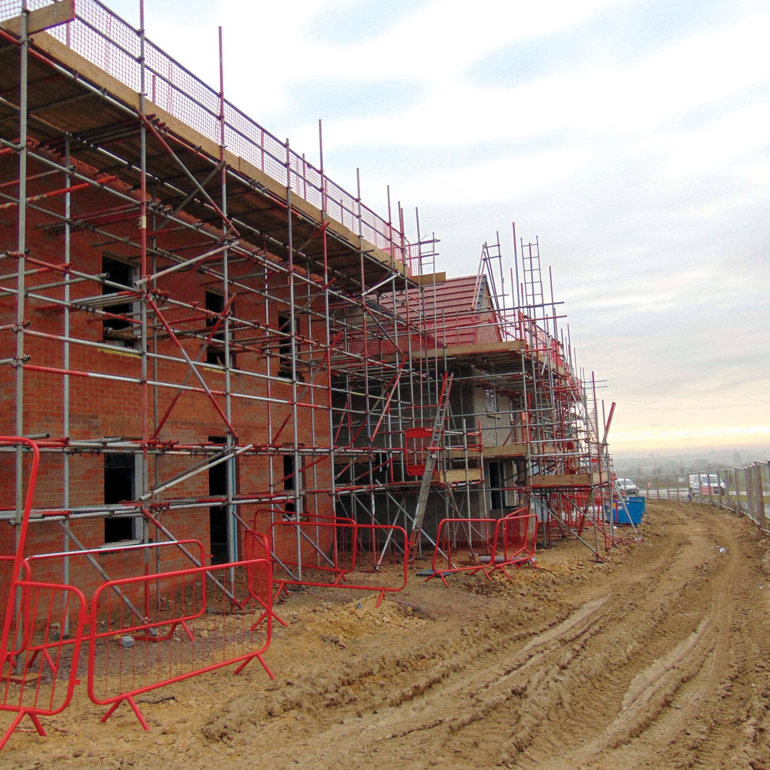 Scaffolded brick houses under construction on muddy site